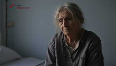 Пожилая женщина сидит на кровати со взглядом в пустоту